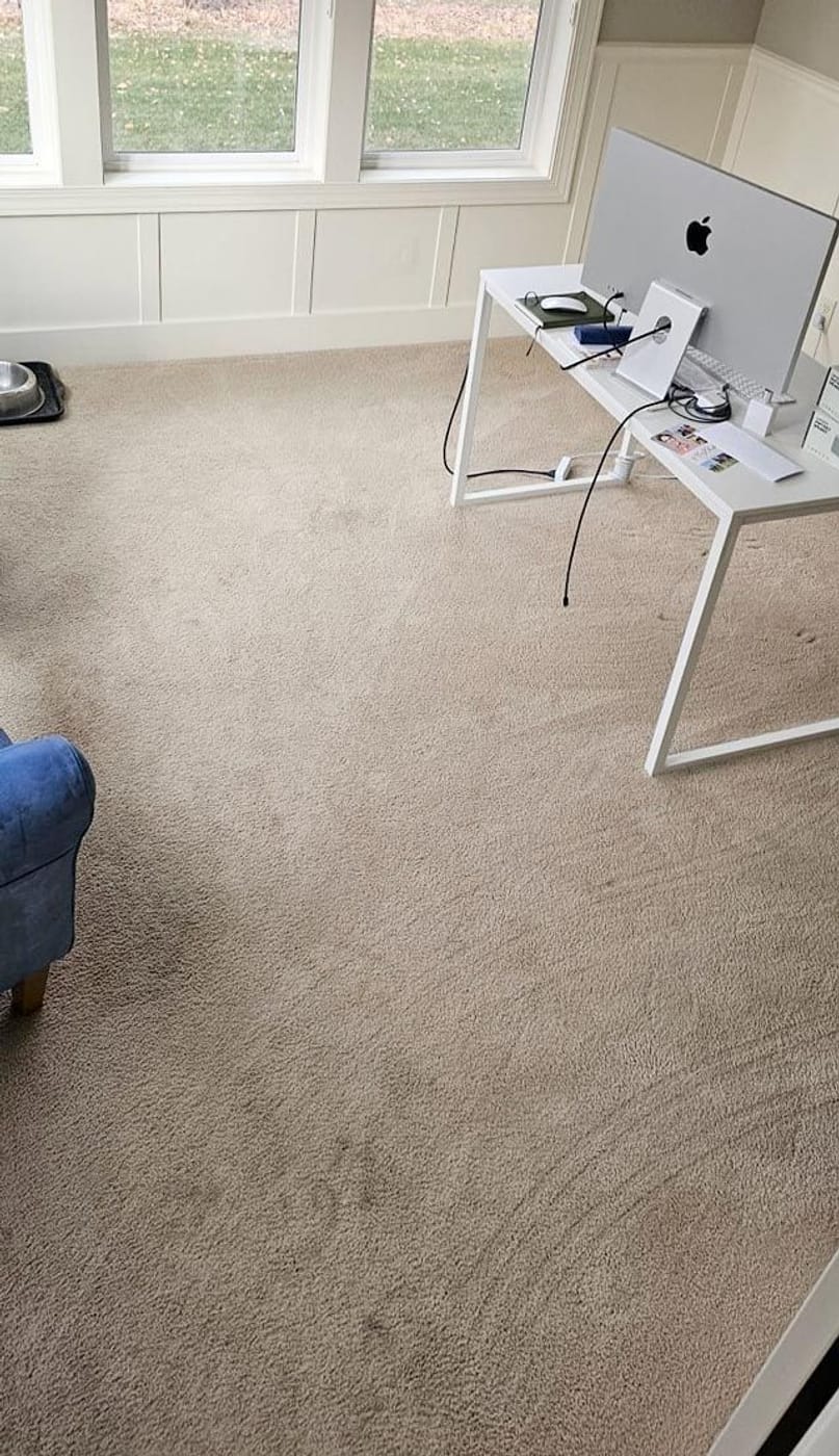 A carpeted office before cleaning, with spotting across the floor in front of the desk